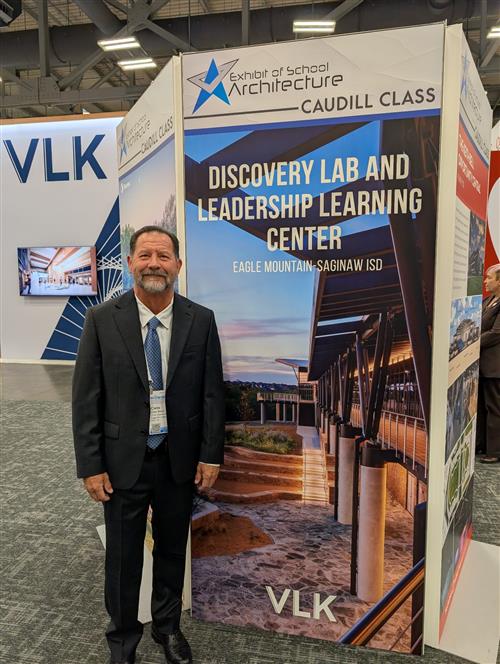 A man stands infant of a large poster of the EMS ISD Discovery Lab