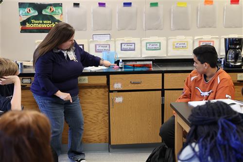A teacher pointes to multi colored liquid