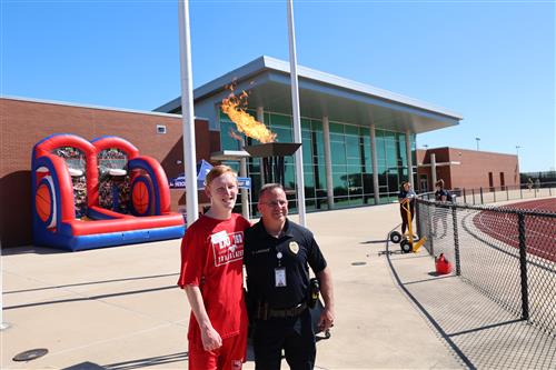 special olympian and police officer with lighted cauldron behind