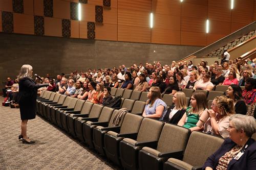 A woman addresses a crowd in an auditorium