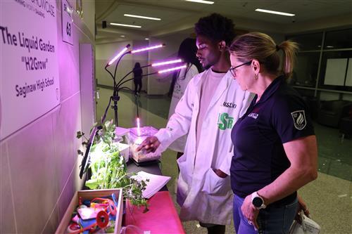 A student and a woman look at plants under a grow light