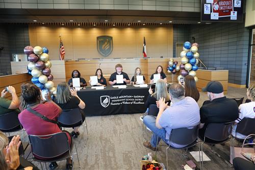 Students hold up certificates while adults clap and take pictures