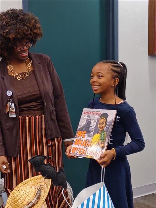 A girl holds the book We Shall Overcome while her mom smiles on