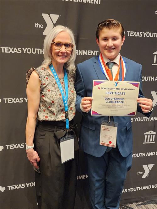 A woman stands next to a boy in a suit holding a certificate