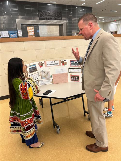 a man in a suit talks with a girl in traditional Afghan dress