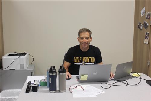 A man sits at a desk and smiles at the camera