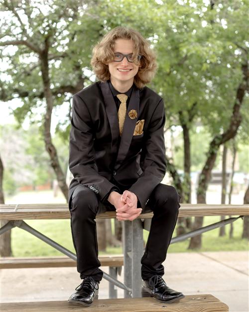 A late teens boy in a suit sits on a bench