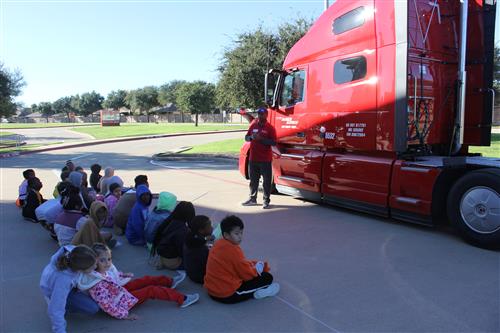 A man with the cab of an 18 wheeler talks to students
