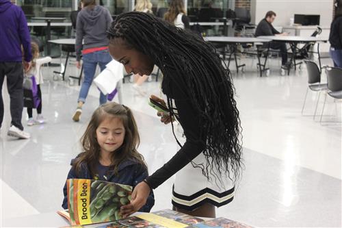 A high school student looks at a book with an elementary student