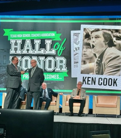 Two men do an interview with a giant screen behind them with pictures