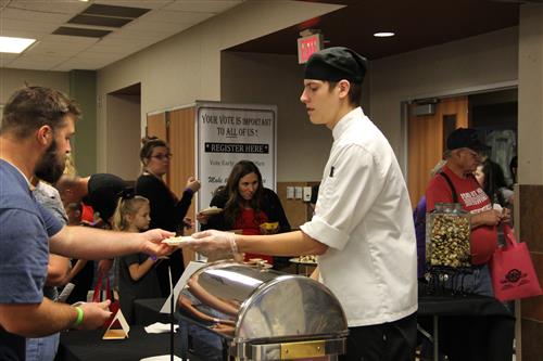 A culinary student serves Casino Dip to a patron. 