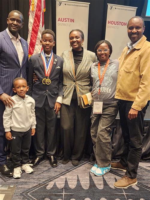 From left to right a man, a little boy, and older boy wearing two medals, a woman, a girl, a man