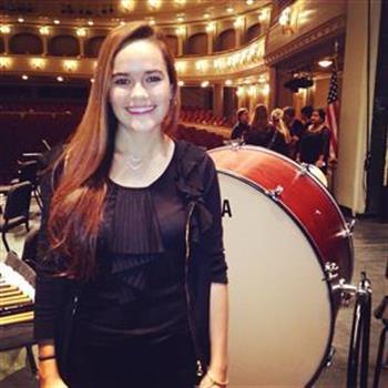 Jenn Giba, percussion director, standing in front of a bass drum in a concert hall 