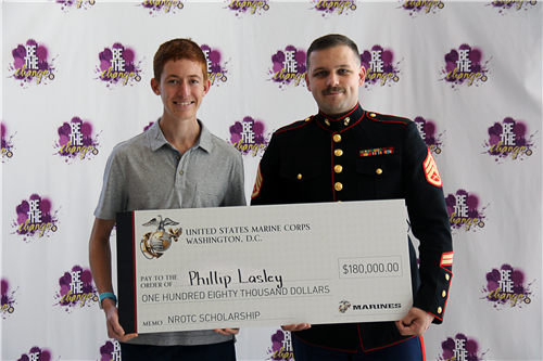 Male students and male marine together holding a large symbolic check