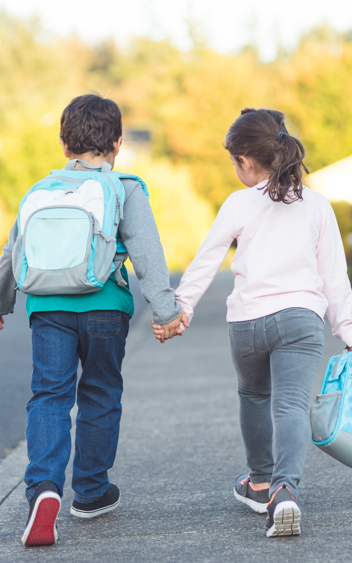 two young students hold hands while walking to school