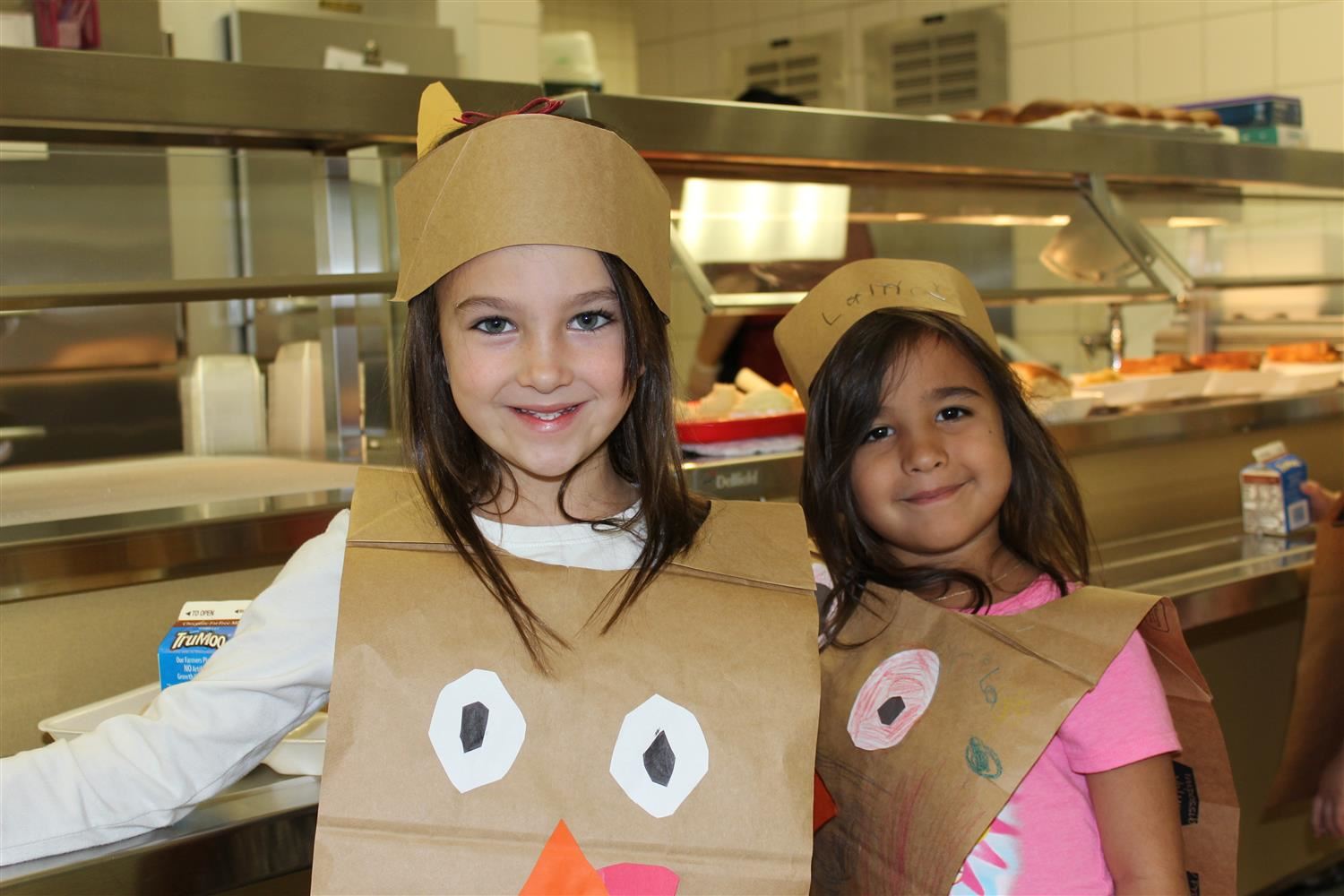 Students smile inside the lunchroom wearing turkey headdress