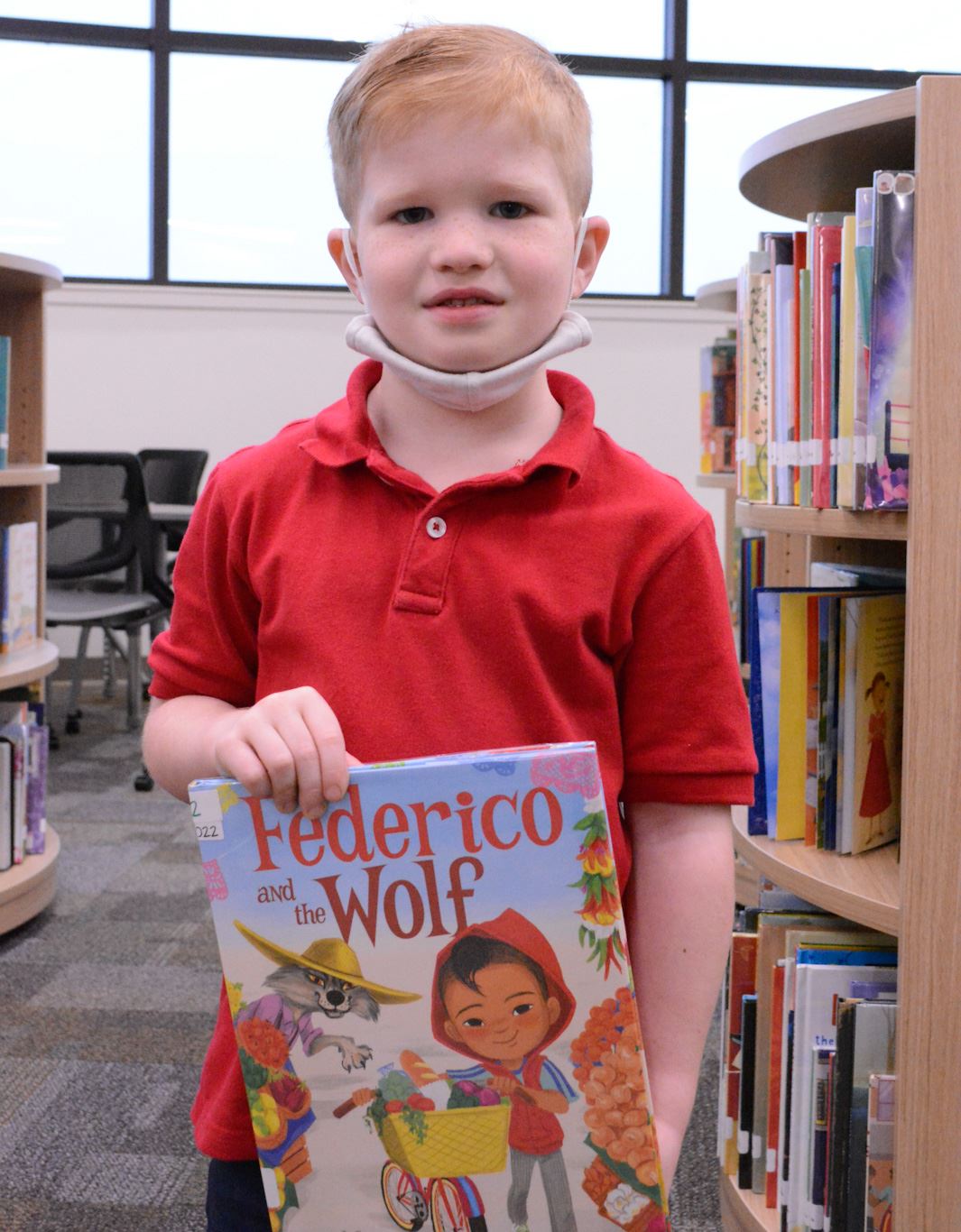 student holds a book and smiles in a library