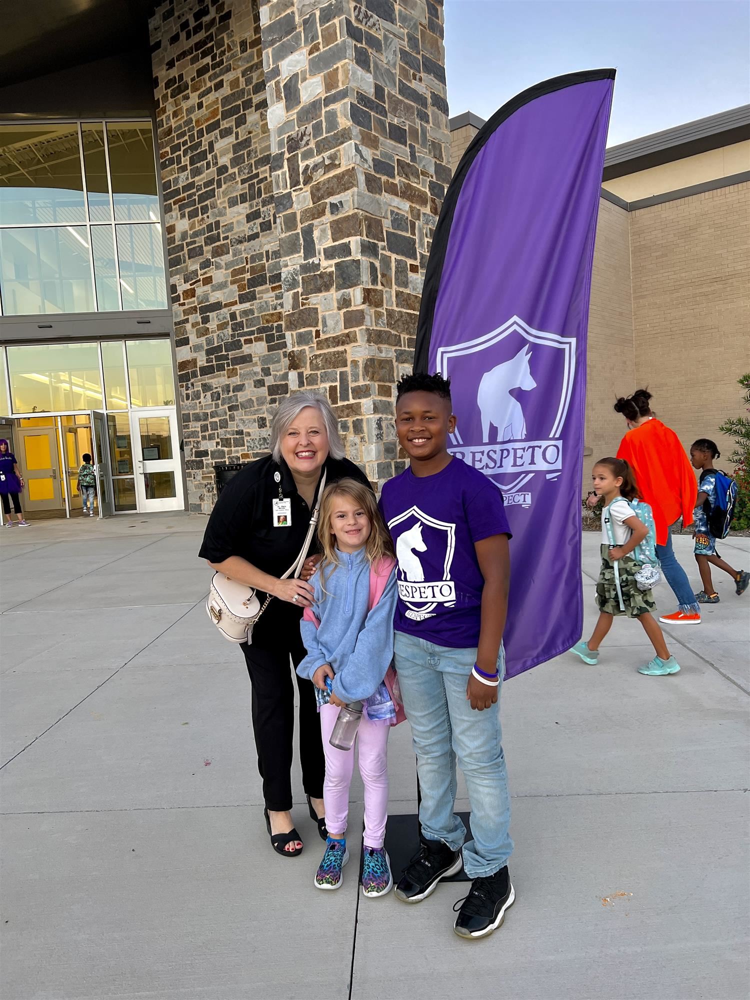 two students pose with district admin in front of Respeto house flag
